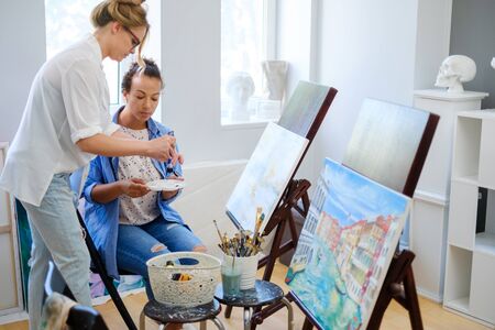 Creative painter and her protege working in a studioの写真素材