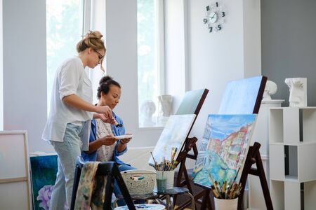 Creative painter and her protege working in a studioの写真素材