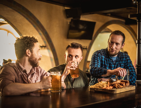 Cheerful friends drinking draft beer in a pubの写真素材