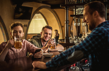 Cheerful friends drinking draft beer in a pubの写真素材