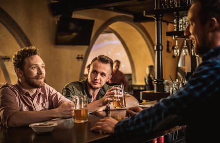 Cheerful friends drinking draft beer in a pubの写真素材