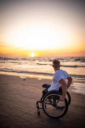 Handicapped man in wheelchair and his girlfriend alone on a beach at sunsetの写真素材