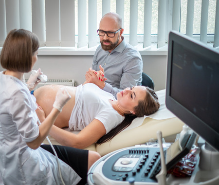 Pregnant woman and her husband on utltrasonographic examination at hospitalの写真素材
