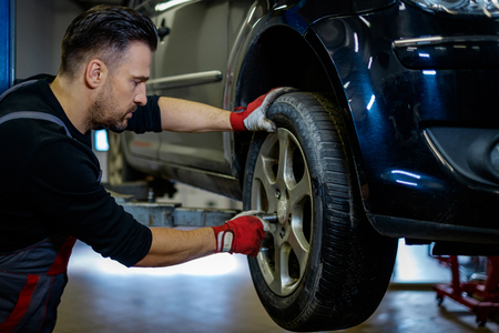 Car mechanic replacing wheel in a workshopの写真素材