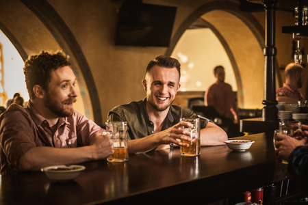 Cheerful friends drinking draft beer in a pubの写真素材