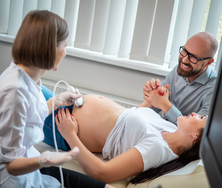 Pregnant woman and her husband on utltrasonographic examination at hospitalの写真素材