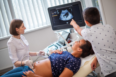 Pregnant woman and her son on utltrasonographic examination at hospitalの写真素材