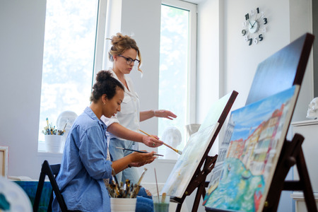 Creative painter and her protege working in a studioの写真素材