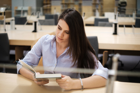 Young woman reading book in public libraryの写真素材