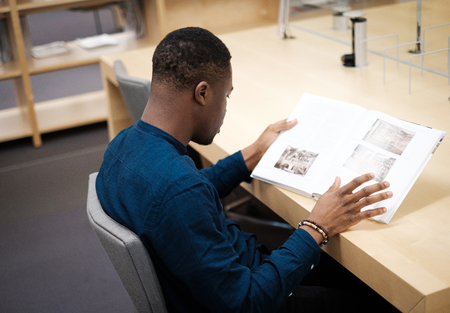 Young man reading book in public libraryの写真素材