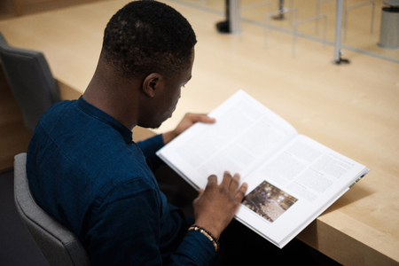 Young man reading book in public libraryの写真素材