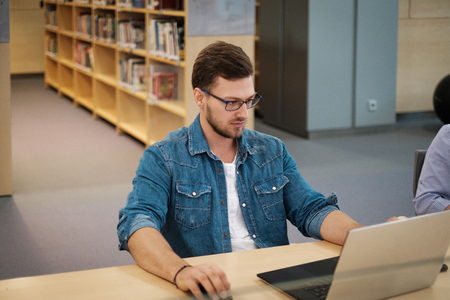 Young man working on a laptop in public libraryの写真素材