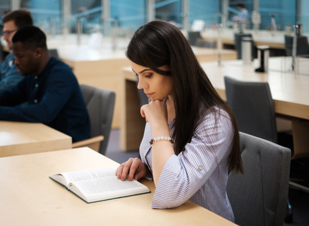 Young woman reading book in public libraryの写真素材