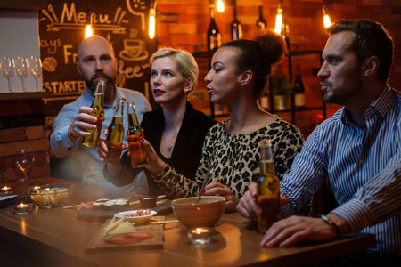 Group of friends watching tv in a cafe behind bar counterの写真素材