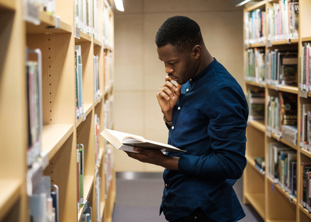 Young black man choosing book in public libraryの写真素材