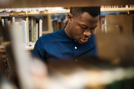 Young black man choosing book in public libraryの写真素材
