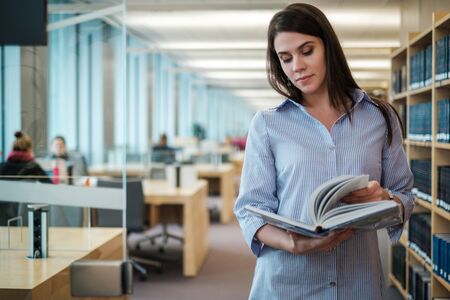 Young woman choosing book in public library