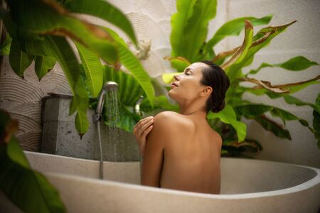 Woman relaxing in outdoor bath with tropical leaves at Baliの写真素材