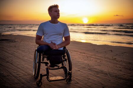 Handicapped man in wheelchair and his girlfriend alone on a beach at sunsetの写真素材