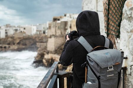 Photographer taking picture of a stormy sea in Polignano a Mare, Italy.