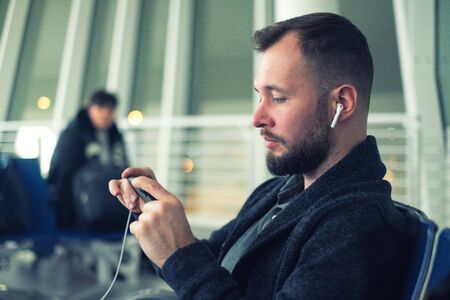 Man wearing wireless earphones looking at screen of smartphone