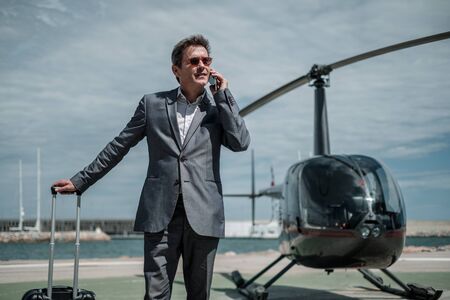 Businessman talking over the phone near private helicopterの写真素材