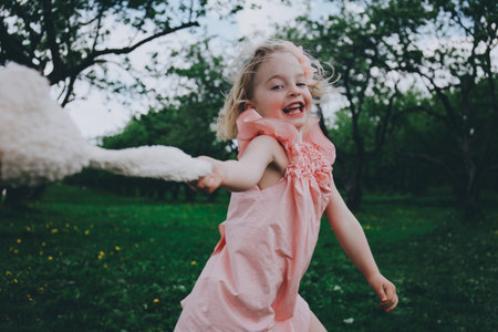 Little cute girl in a pink dress running on the grass with toy rabbit.の写真素材