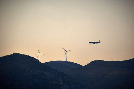airplane flying over wind turbines in mountain scenery の写真素材