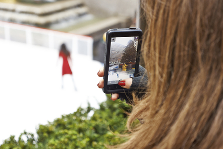 tourist taking picture with smartphone of people ice skating at rockefeller centerの写真素材