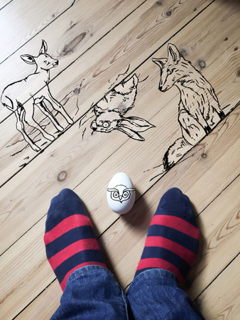 Drawings of aninmals on wooden floor. Bambi, fox and rabbit drawn on the floor, animals look towards the egg. Head of an owl directly on the egg. Egg is in between my feet.の写真素材