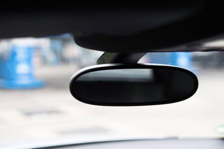 Detailed view of a black driving mirror in a car. The background is and the reflections in the...
