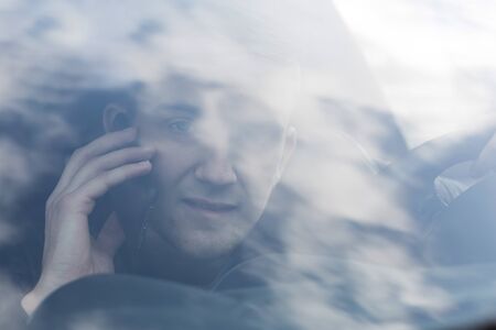 portrait of young adult behind steering wheel inside a car making a phone call with his smartphone