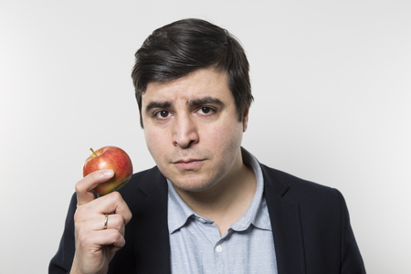 Dark-haired european businesmann with a serious look hold an small apple while in front of a gradient backgroundの写真素材