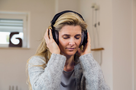 people, technology and leisure concept - happy middle-aged woman sitting on sofa with smartphone and headphones listening to music at homeの写真素材