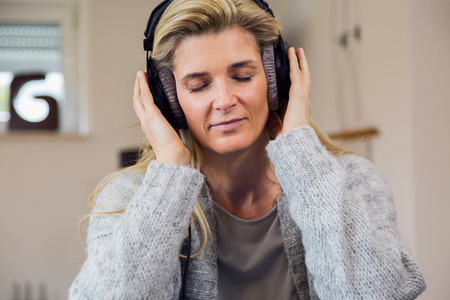 people, technology and leisure concept - happy middle-aged woman sitting on sofa with smartphone and headphones listening to music at homeの写真素材