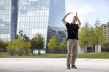 A man making hand gestures while standing in front of modern glass building.