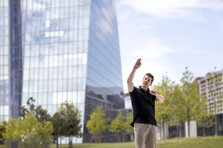 A man making hand gestures while standing in front of modern glass building.の写真素材
