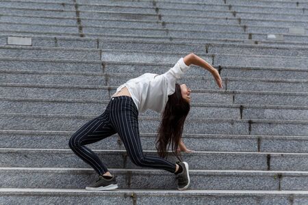 Young woman in back stand position on marble steps. Profile view. Full length.