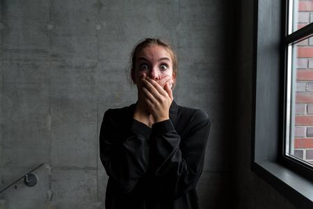 Young Woman with Shocked Facial Expression Covering Mouth with Hands