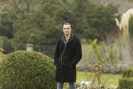 Young Man Listening to Earphones Posing in Topiary Gardenの写真素材