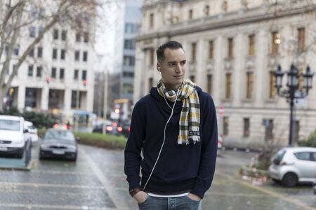 Young Man with Earphones and Head Turned in Urban Settingの写真素材