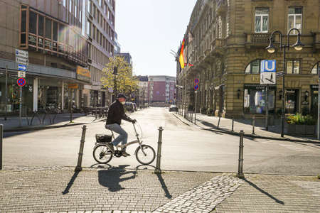 Coronavirus lockdown. Frankfurt, Germany. April 5, 2020. Old man riding bicycle on empty street wearing a mask. Profile view.のeditorial素材