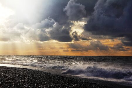 Sunset over sea with dramatic sky sky, dark storm clouds, and red light. Stormy weather.の写真素材