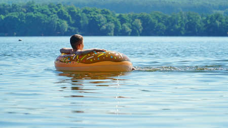 An orange rubber ring floats on the river, in which the child sits, ecotourism in the river ecosystem, outdoor recreation. Carefree happy childhood. Summer. A man swims in an inflatable circle.の写真素材