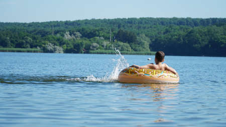 An orange rubber ring floats on the river, in which the child sits, ecotourism in the river ecosystem, outdoor recreation. Carefree happy childhood. Summer. A man swims in an inflatable circle.の写真素材
