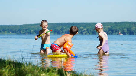 A happy and carefree childhood. Happy kids play with water guns in the water. Warm summer. Children's emotions. nのeditorial素材