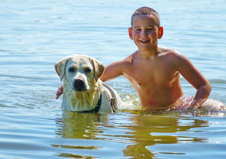A happy and carefree childhood. Happy boy with a dog swims in the water. Golden retriever, a labrador plays with a child in the water. nのeditorial素材