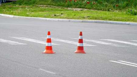 Macro shot of road traffic cones with orange and white stripes standing on street on gray asphalt during road construction works. Just painted white street lines on pedestrian crossingの写真素材