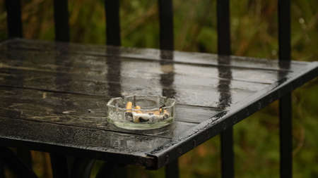 Glass ashtray. Wet ashtray with extinguished cigarettes on the table after the rain. Bad habits...