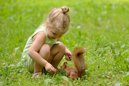 Kid girl feeds squirrel in the parkの写真素材